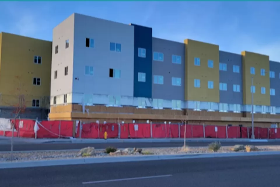 White, yellow, gray boxy apartment building with construction fence surrounding bottom floor in Albuquerque, New Mexico.